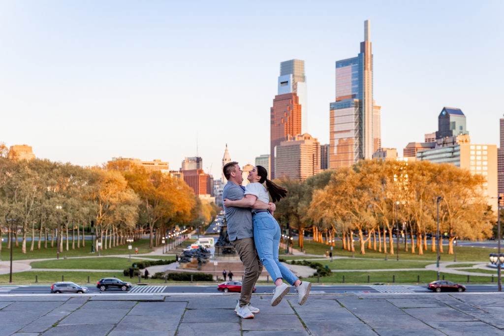 A couple spins in each other's arms on the Art Museum Steps overlooking the Philly skyline during an engagement session.