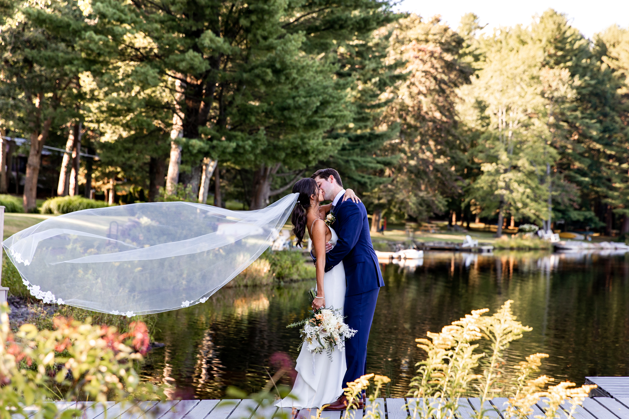 a bride and groom kiss on a dock at a lake in the poconos, pa