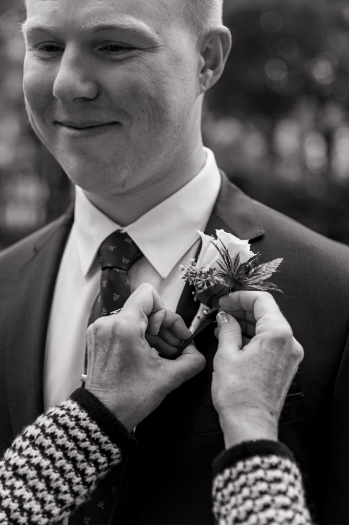 mother of the groom pinning a boutonnière on her son