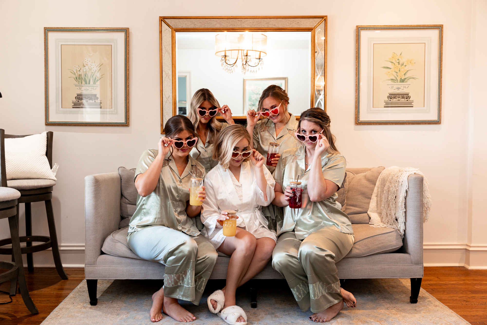 Bride and her Bridesmaids getting ready wearing silk robes and heart-shaped sunglasses sitting on a couch