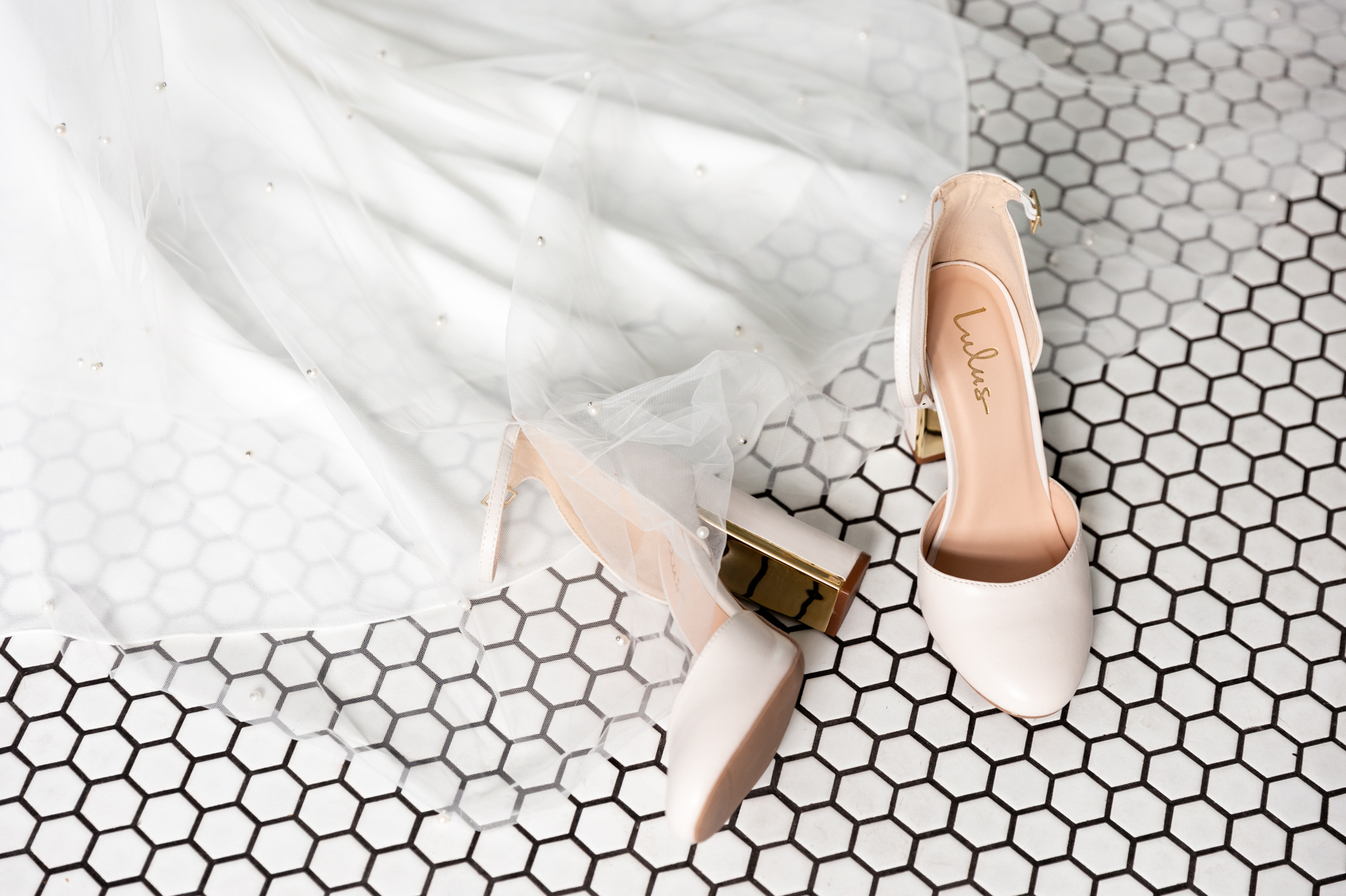 Nude wedding shoes and wedding dress train against black and white penny tile floor