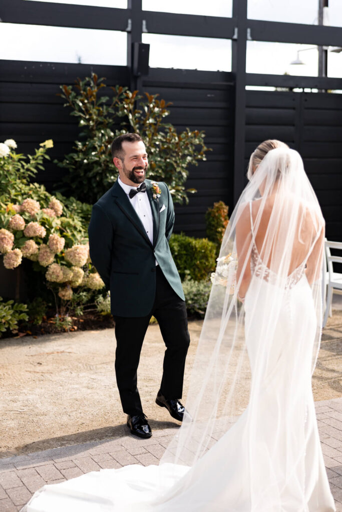 A groom smiles as he sees his bride for the first time on wedding day during their first look at Terrain Gardens in Devon, PA.