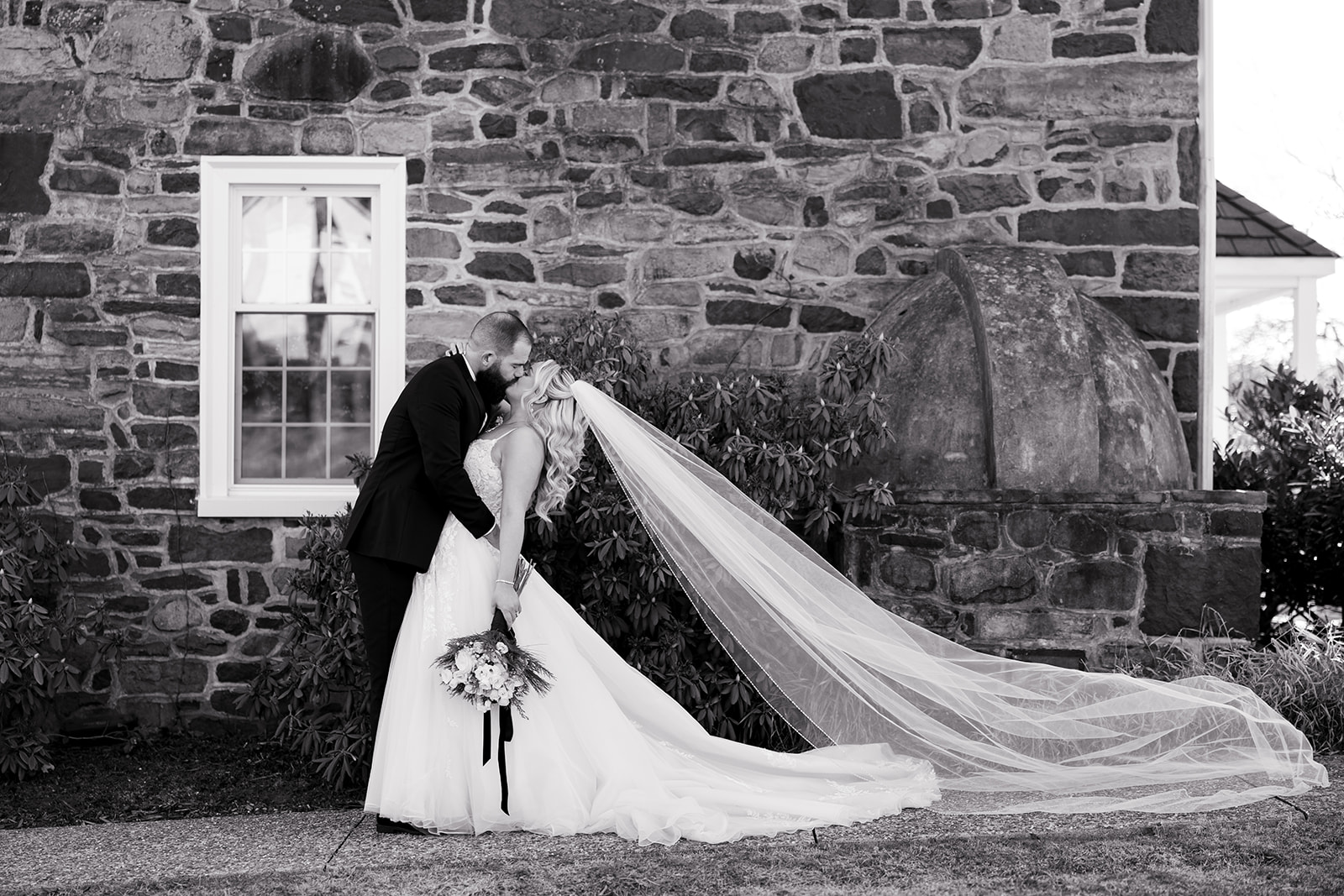a bride and groom dip into a kiss with the bride's cathedral-length veil trailing behind her during a wedding at La Massaria at Bella Vista.